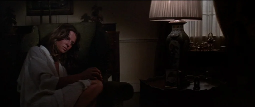 Demon Seed (1977) movie still: medium — An interior space features an upholstered chair and a decorative lamp on a table. A woman in a white sweater…