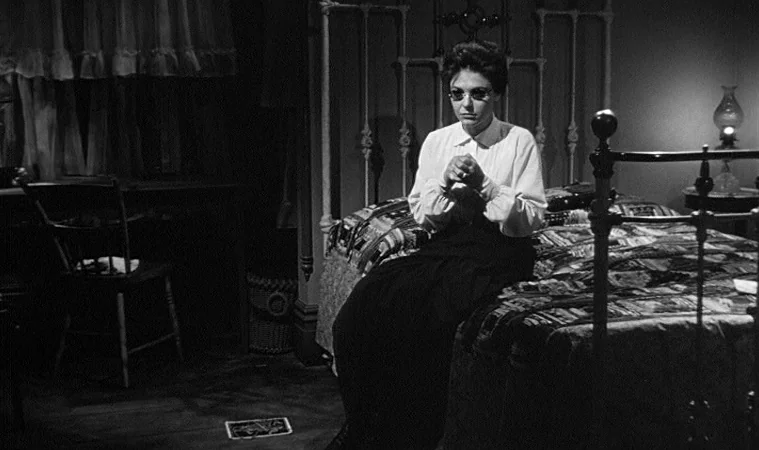 The Miracle Worker (1962) movie still: medium — A dark, sparsely furnished room features an iron bed frame and an old oil lamp. A woman sits on the…