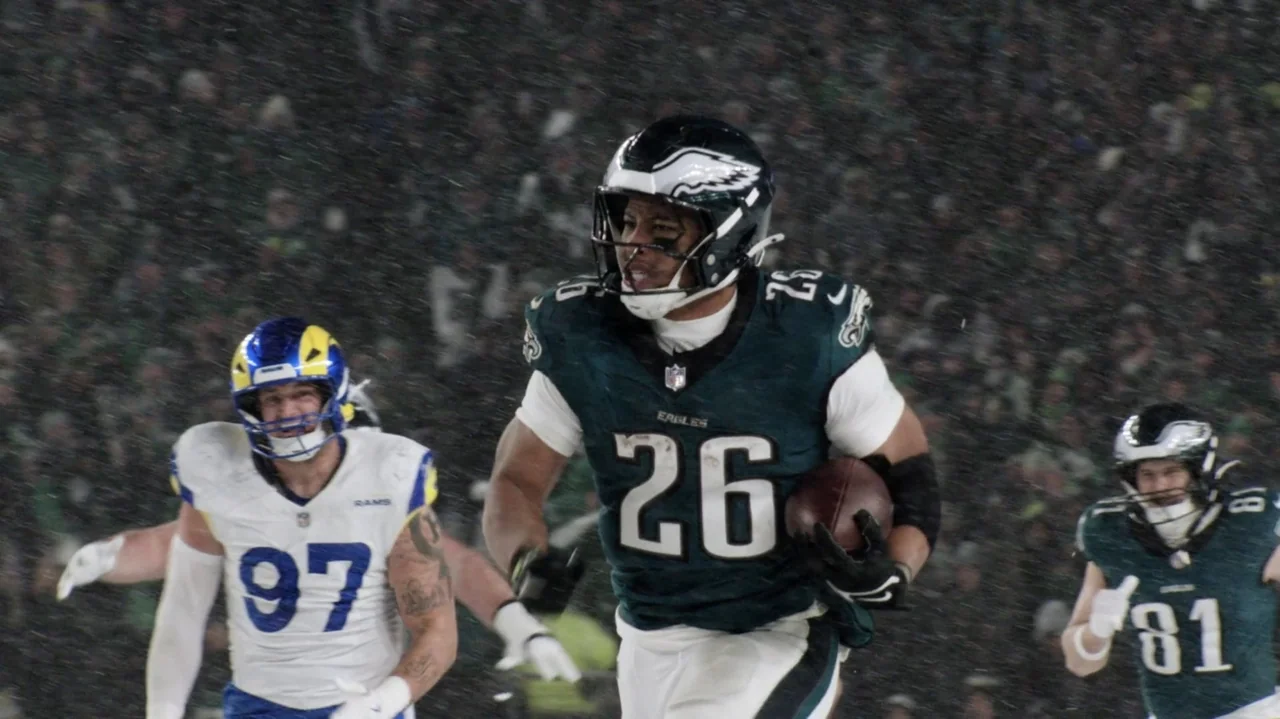 SAQUON (2025) movie still: medium — A rain-slicked professional football field at night under bright stadium lights. A running back carries the ball…