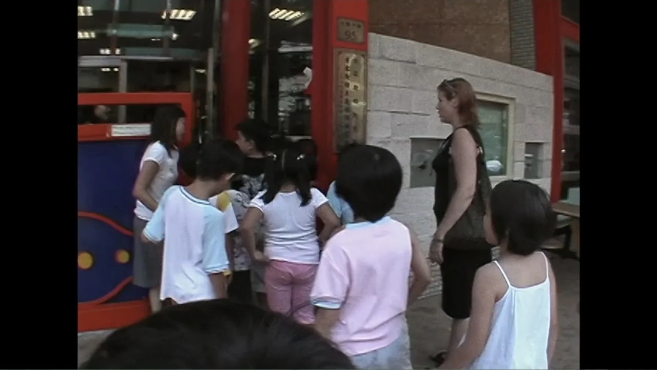 Daniel (1983) movie still: medium — A group of children and an adult woman stand at a red-framed doorway. The group is gathering near a concrete…