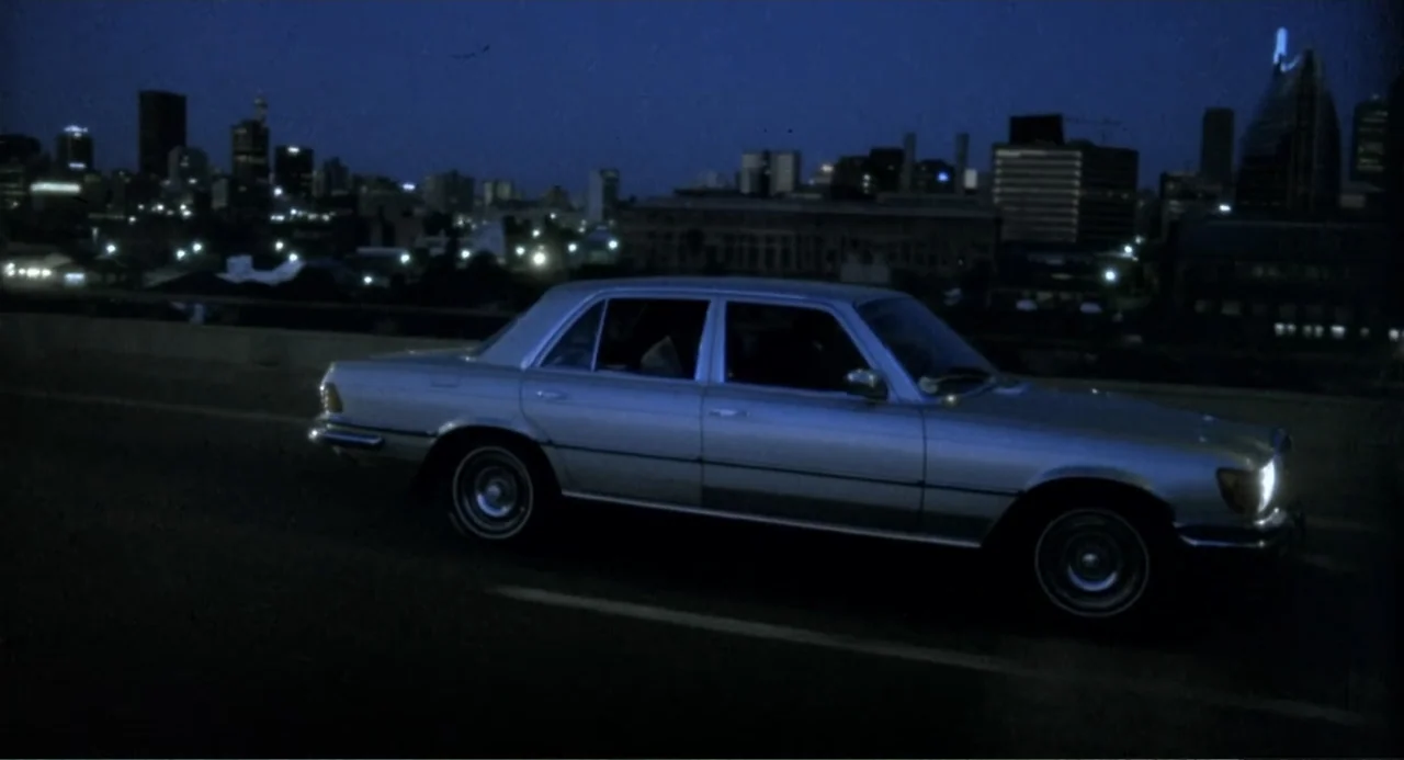 American Ninja 3: Blood Hunt (1989) movie still: wide — A dark urban highway bridge spans across a sprawling city skyline at night. A silver sedan…