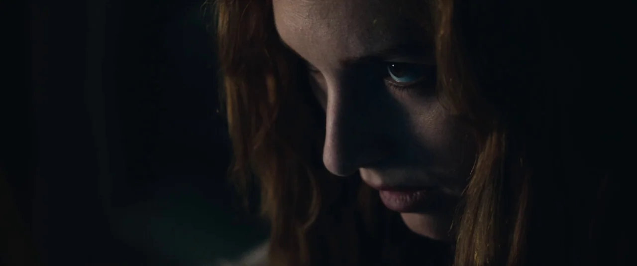 Kiss of the Damned (2012) movie still: closeup — A dark, minimally lit room serves as the setting for the subject. A woman looks down at an object…