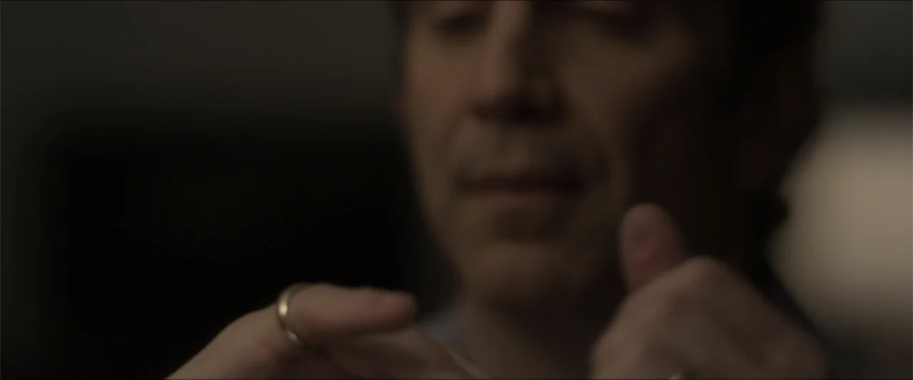 Heavenly Deposit (2019) movie still: closeup — A dimly lit indoor space with the foreground focus on a person's hands. The subject is out of focus…