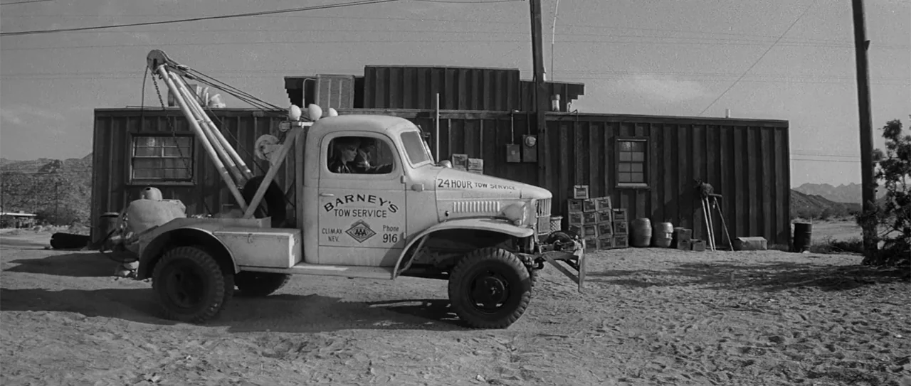 Kiss Me, Stupid (1964) movie still: medium — A vintage white tow truck is parked in front of a weathered wooden building. A woman sits in the…
