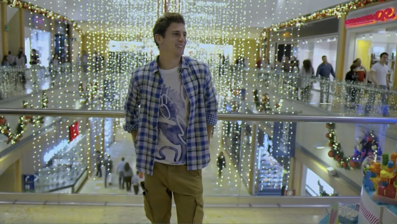 Loco Love (2003) movie still: medium — A man stands on a mall balcony overlooking the interior levels filled with festive lights. He gazes…