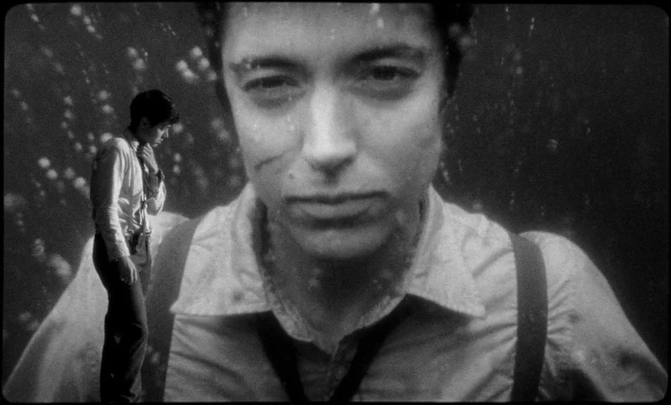 The Wild Boys (2017) movie still: closeup — A dark, aquatic environment filled with floating bubbles and suspended particles. A person in a shirt…