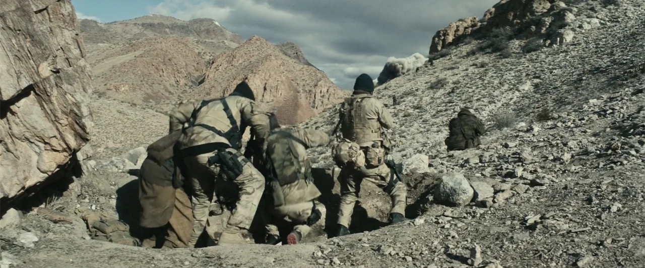 12 Strong (2018) movie still: wide — A desolate rocky hillside features arid terrain with sparse vegetation and a dust cloud. Four soldiers in…