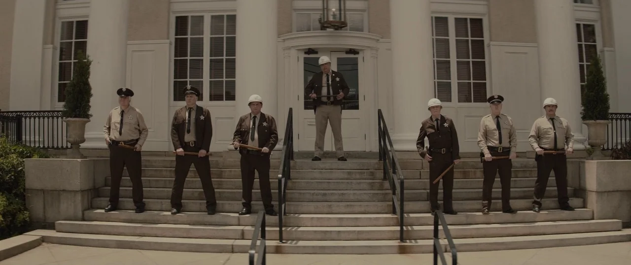 Selma (2014) movie still: fullbody — Seven police officers stand in a horizontal line on the wide stairs of a building. They wear tan or brown…