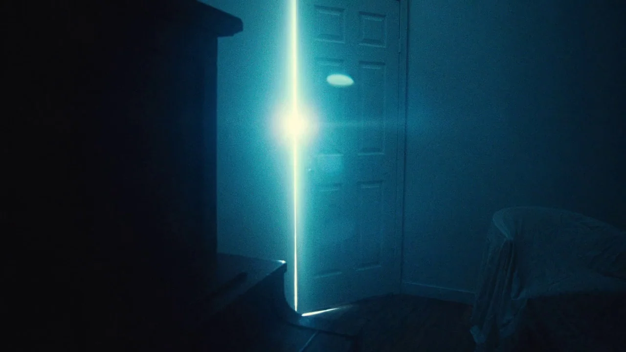 Love & Mercy (2014) movie still: establishing — A dimly lit room with plain walls and dark furniture is bathed in cool shadows. A door is slightly…
