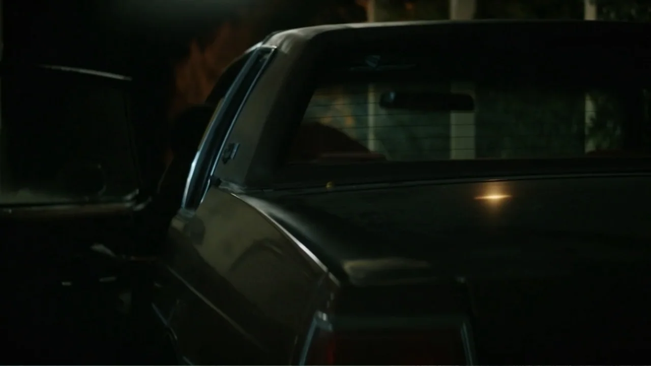 Nightingale (2014) movie still: medium — A dark sedan sits parked in a dim outdoor setting at night. The driver side door is open with the interior…