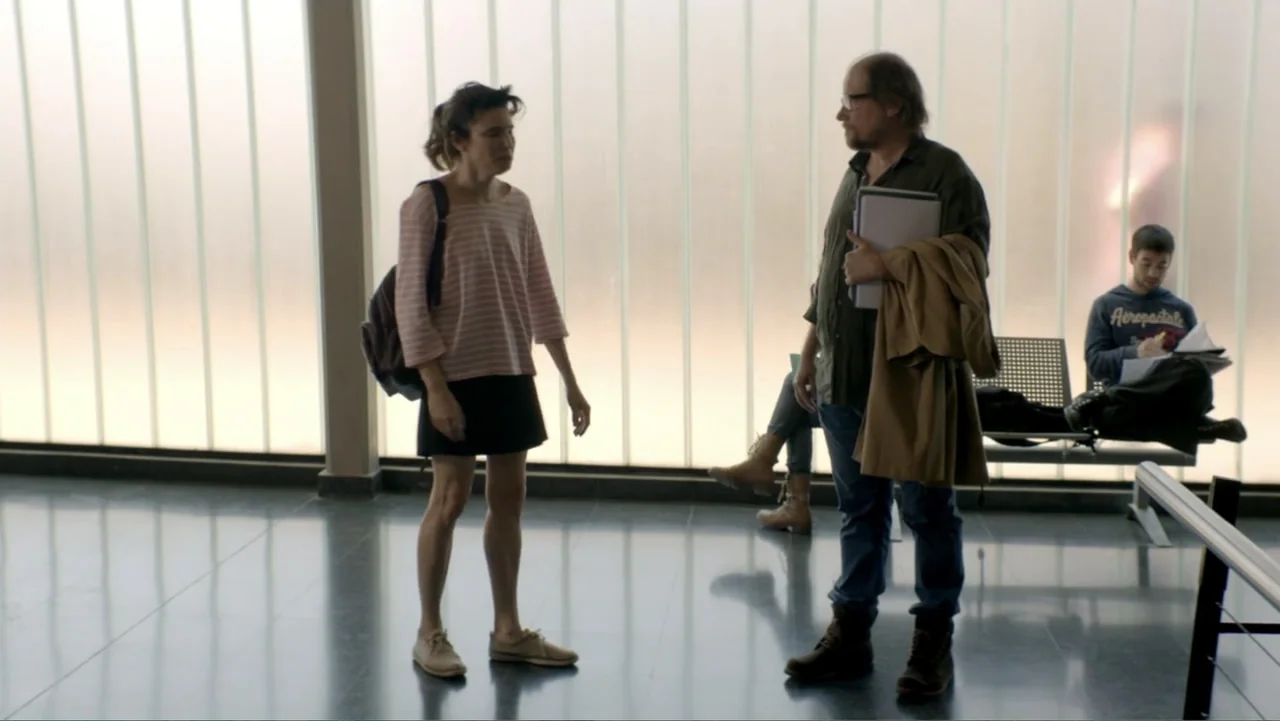 I Married a Dumbass (2016) movie still: fullbody — An interior waiting area features floor-to-ceiling translucent glass panels and polished dark…