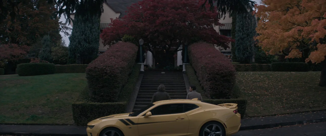 Pig (2021) movie still: wide — A suburban property with a wide stone staircase leading up to a large house. Two men walk toward the front door while…