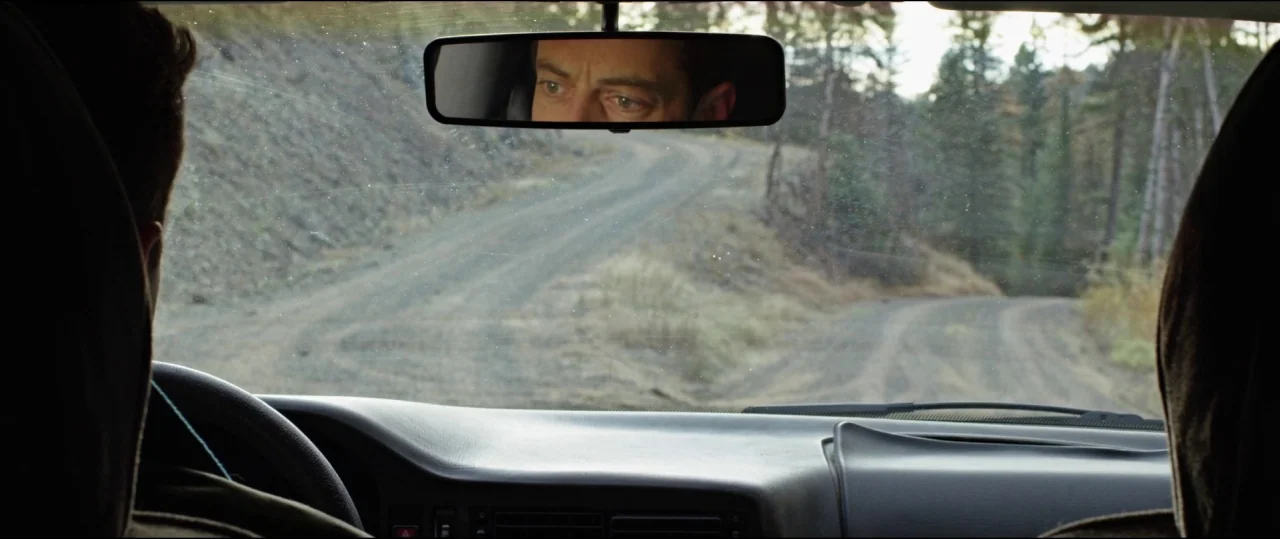 Buster’s Mal Heart (2016) movie still: medium — A view from the interior of a car looking out onto a dirt road. A male driver is visible through the…