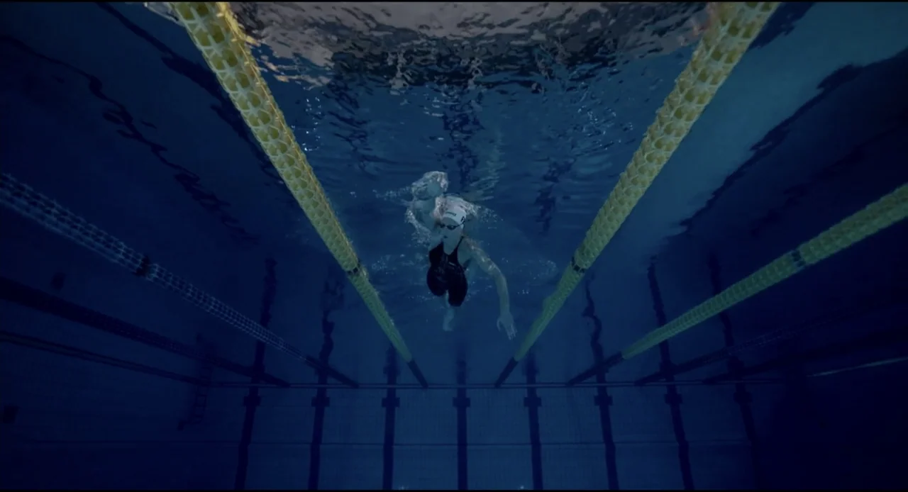Federica Pellegrini - Underwater (2022) movie still: wide — An underwater view of a competition pool with yellow lane lines stretching across. A…