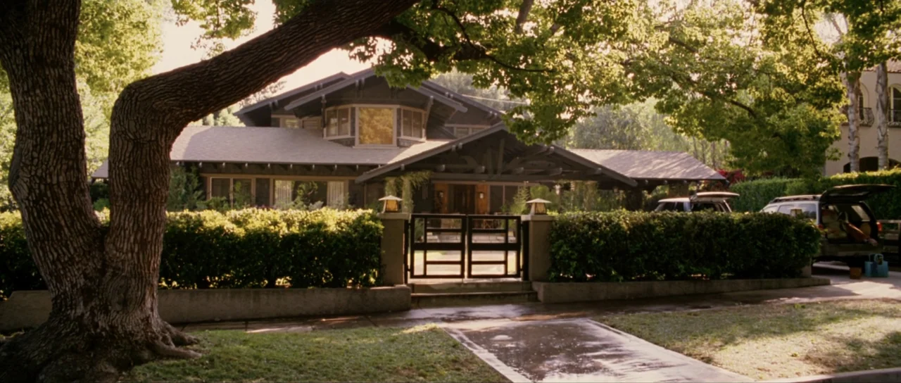 Monster-in-Law (2005) movie still: establishing — A dark wooden craftsman style house sits behind a thick green hedge. Two cars are parked in the…
