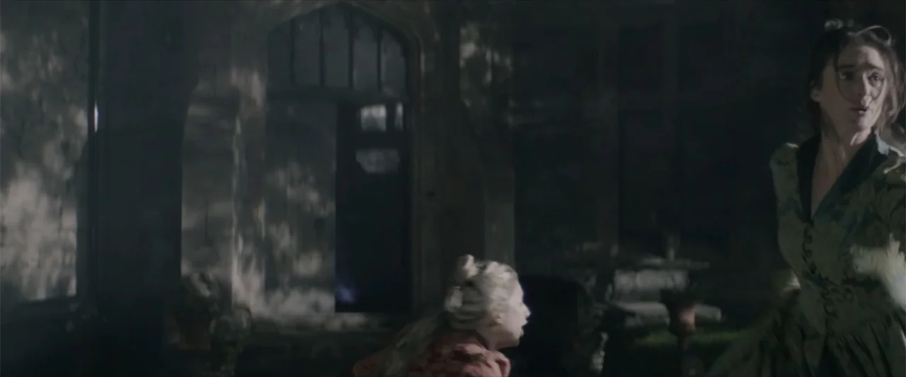 Cinderella's Curse (2024) movie still: medium — A dark stone courtyard of an old estate features gothic doorways and textured masonry. A woman in a…