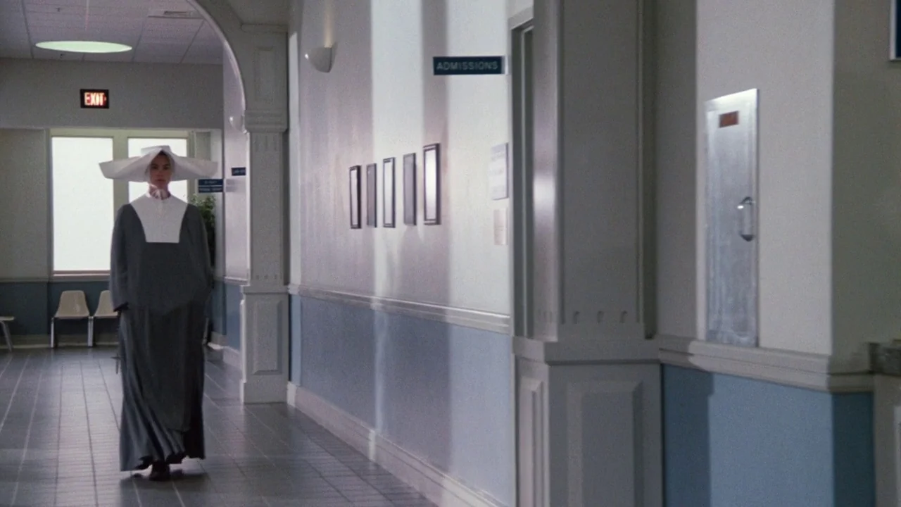 The Exorcist 3 (1990) movie still: fullbody — A long hospital corridor features light blue wainscoting and framed art on the wall. A woman in a…