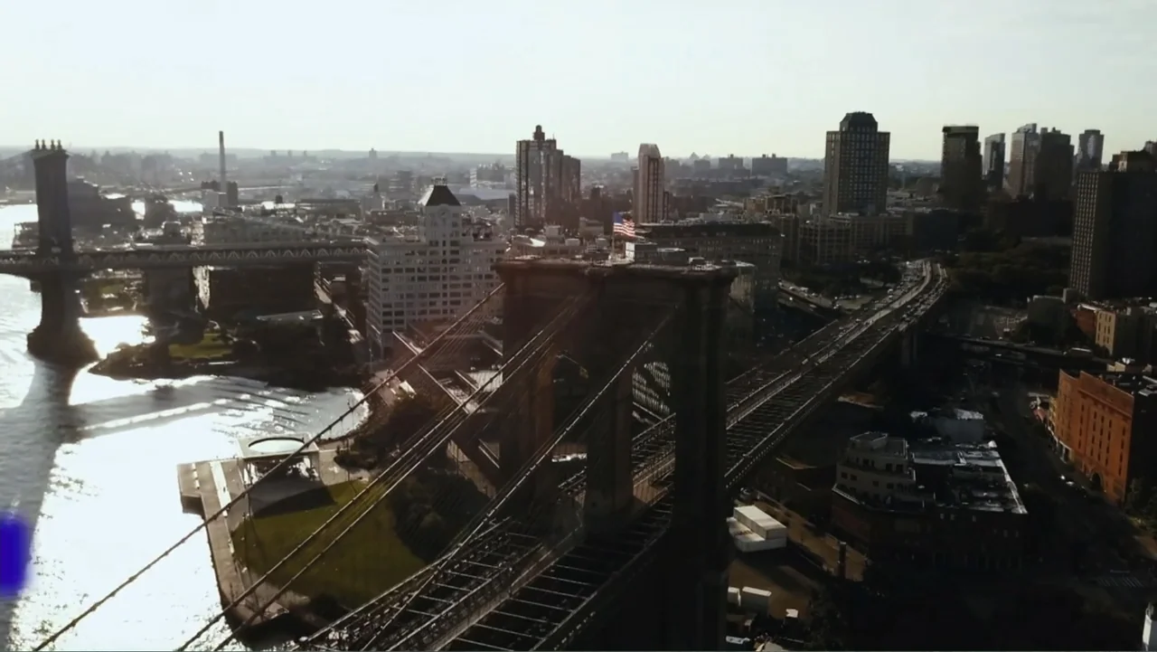 Reign of the Superwomen (2021) movie still: establishing — A high-angle aerial view of the Brooklyn Bridge and the surrounding New York City…