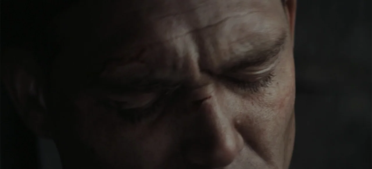 The Tank (2025) movie still: closeup — A dark indoor space where the subject's face occupies most of the frame. A middle-aged man with a scar above…