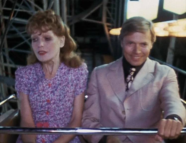 Martha (1974) movie still: medium — A woman and a man sit inside the metal cabin of an amusement ride. The structural steel of the ride is visible…