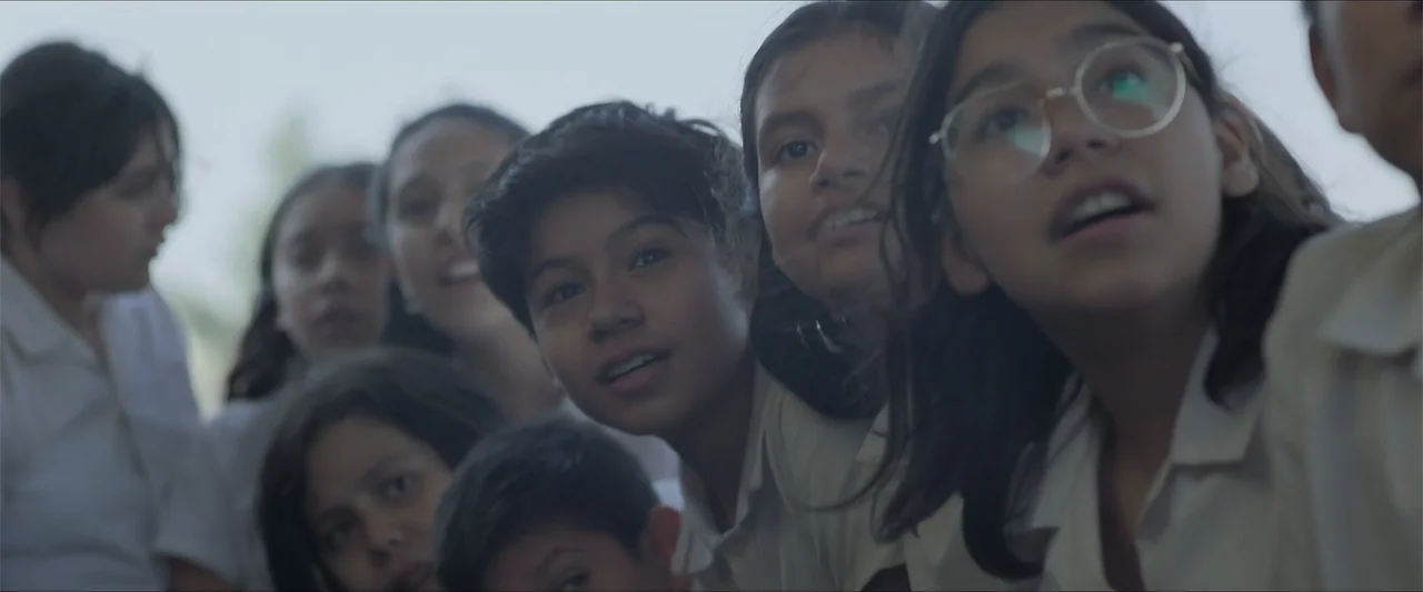 Radical (2023) movie still: medium — A group of young students wearing white uniforms stand outdoors under overcast sky. The children look upward…
