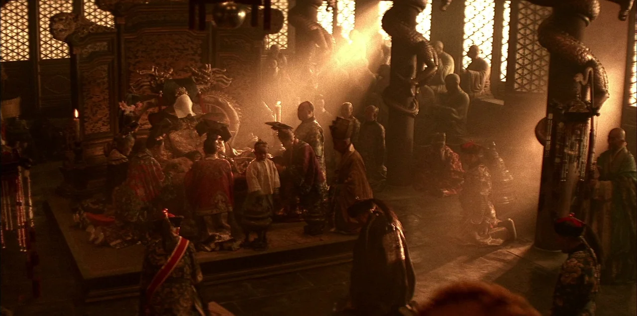 The Last Emperor (1987) movie still: wide — A dark, atmospheric hall with ornate carved wooden pillars and lattice window screens. Numerous figures…