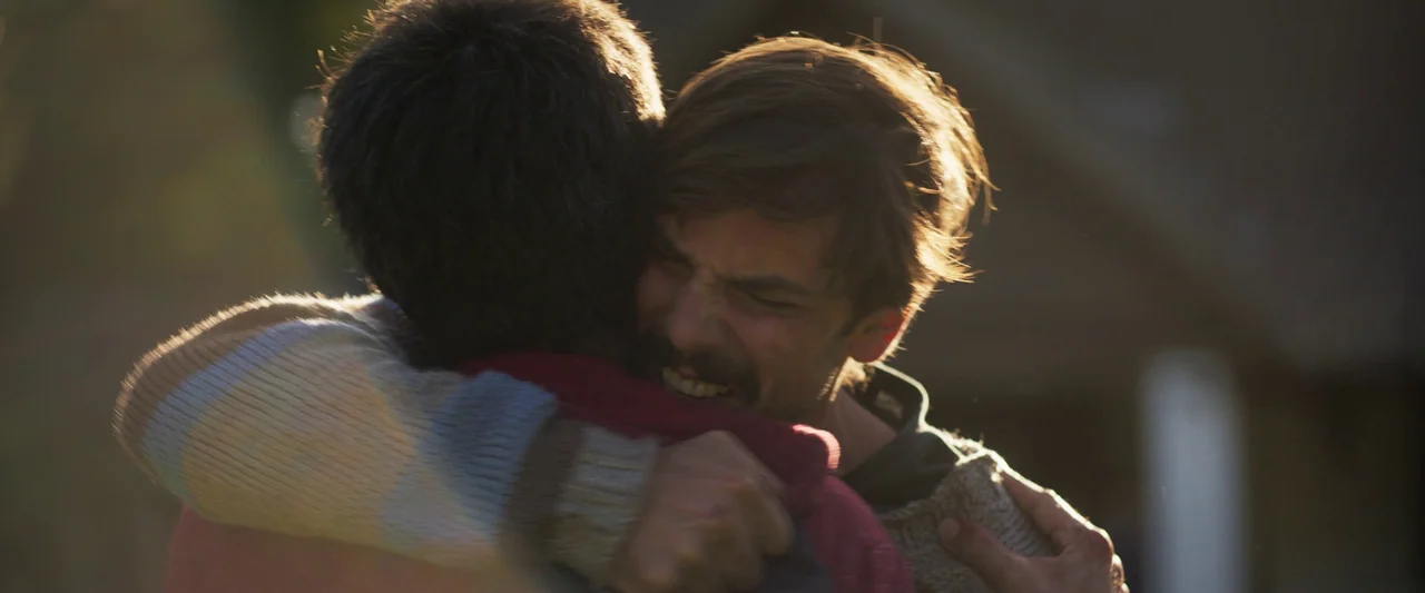When Evil Lurks (2023) movie still: closeup — Two men are in an outdoor setting illuminated by low golden sunset light. The man in the grey sweater…