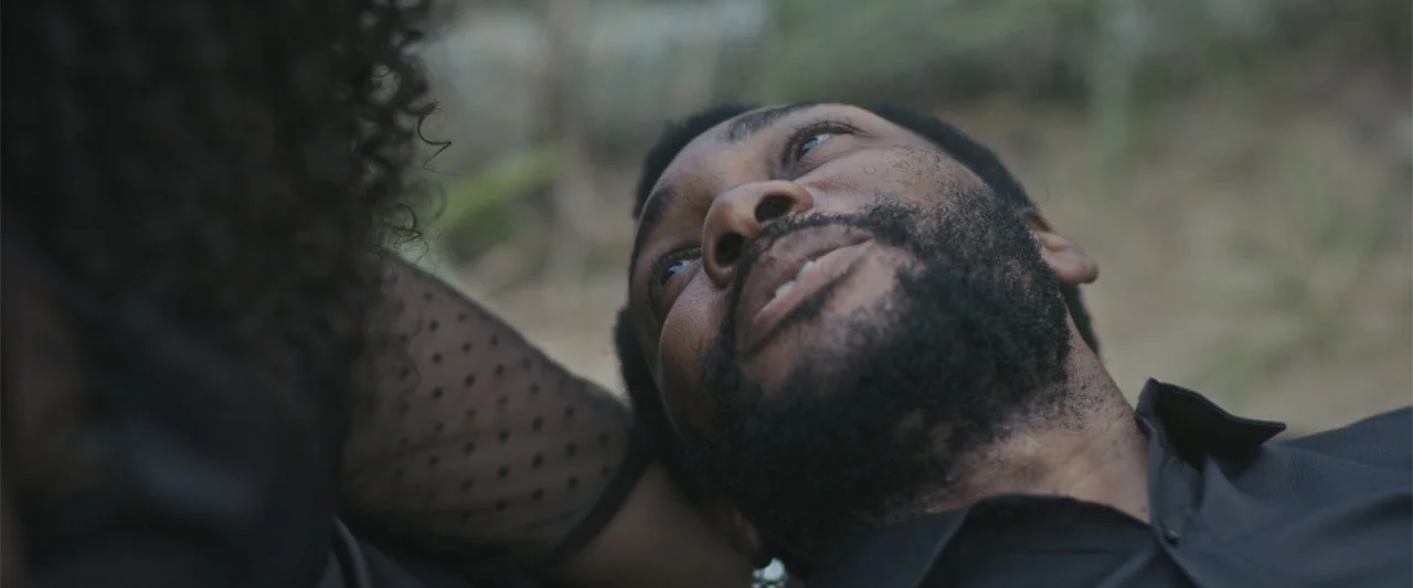 Casa De Novia (2024) movie still: closeup — An outdoor location with blurred green foliage visible in the out-of-focus background. A man and woman…