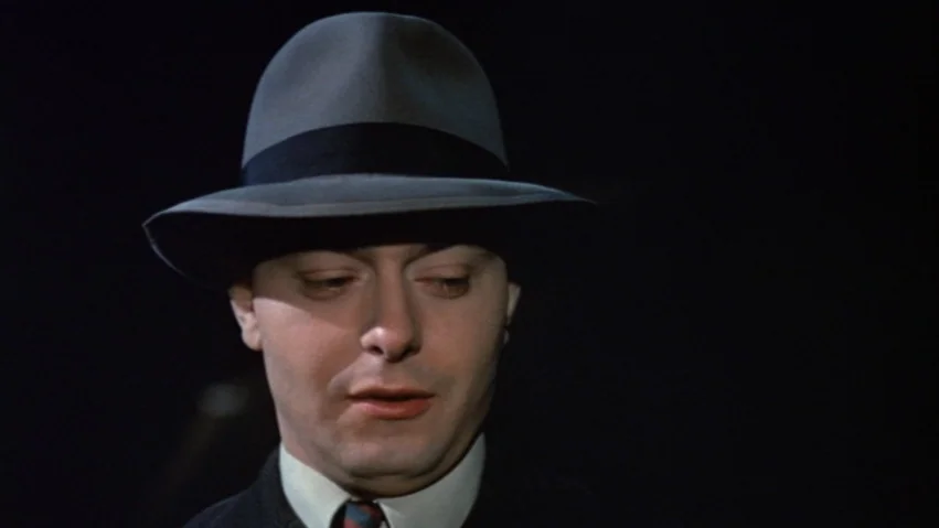 Tenderness of the Wolves (1973) movie still: closeup — A man in a fedora appears against a pitch-black background with no visible surroundings. He…