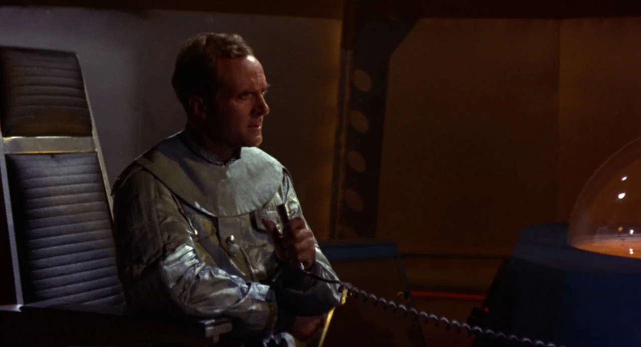 Queen of Blood (1966) movie still: medium — The interior of a spaceship cockpit features a dark console with a glass dome. A man in a metallic…