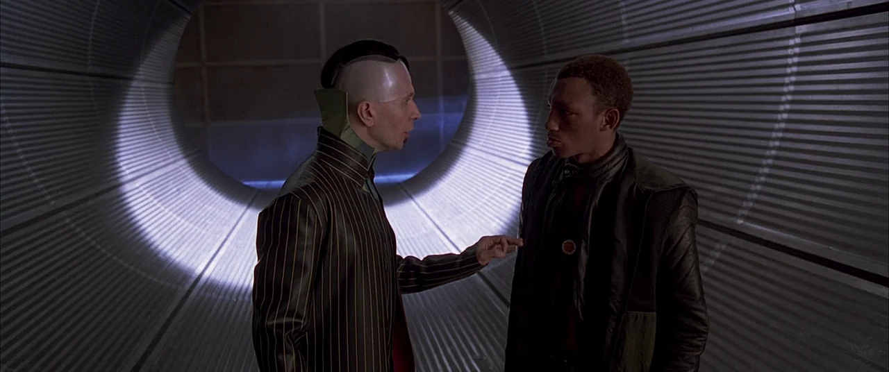 The Fifth Element (1997) movie still: medium — A curved tunnel constructed from ribbed corrugated metal walls creates a narrow path. One man…
