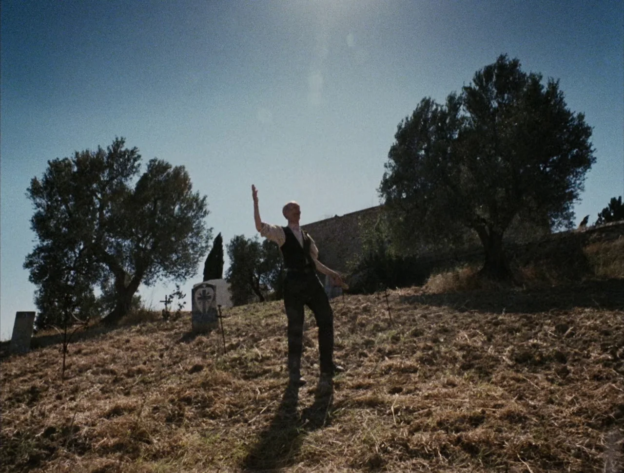 Christ Stopped at Eboli (1979) movie still: fullbody — A dry, grassy hillside cemetery under a clear, bright sky. An elderly man in period clothing…