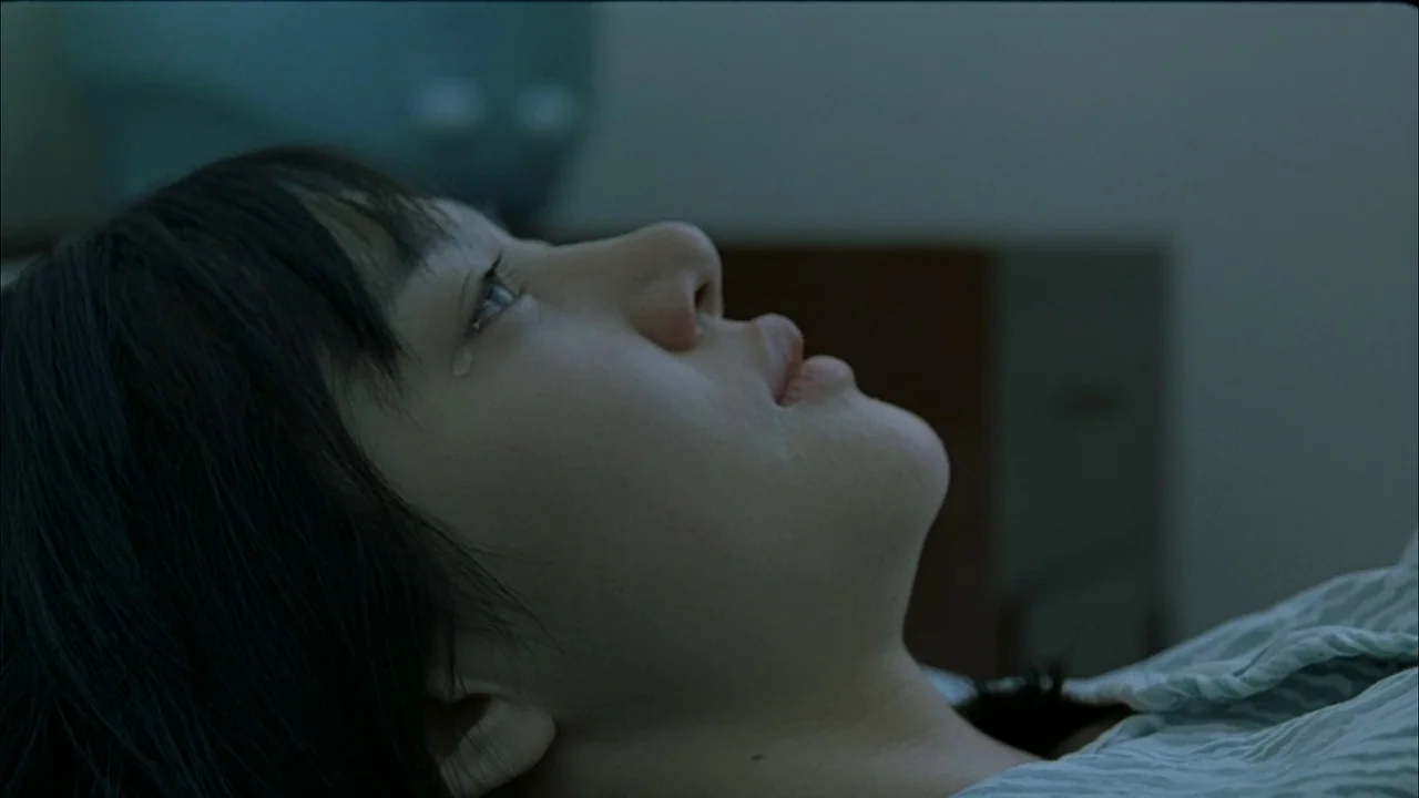A Tale of Two Sisters (2003) movie still: closeup — A clinical space with a neutral wall and indistinct hospital furniture in the background. A…