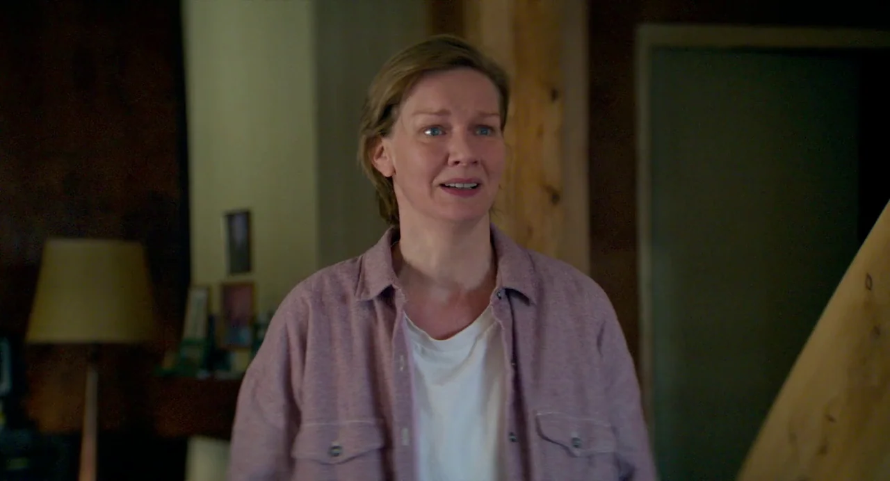 Anatomy of a Fall (2023) movie still: medium — A residential interior features dark wood paneling and a blurred lampshade in the background. A woman…
