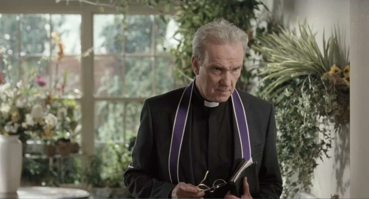 Death at a Funeral (2010) movie still: medium — A light-filled sunroom features large windows filled with indoor plants and floral arrangements. An…