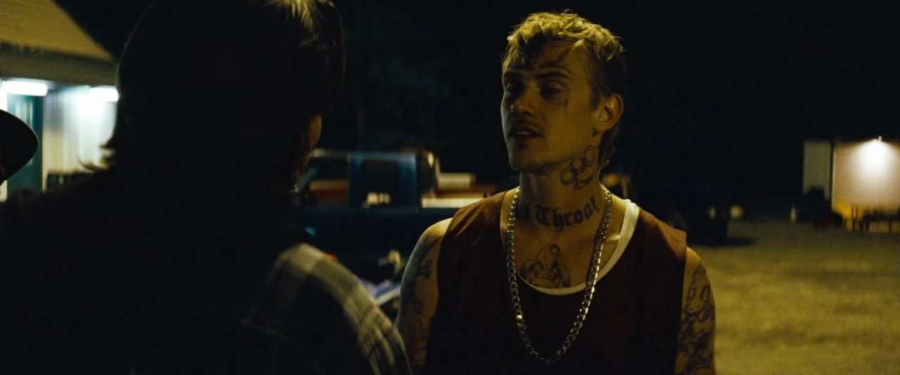 Out of the Furnace (2013) movie still: medium — A dark outdoor parking lot at night with a blue truck visible in the distance. A man with neck…