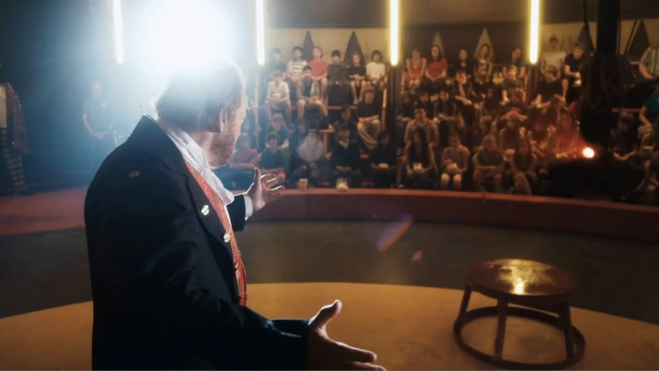 Sophie & Sheba (2010) movie still: medium — A circus ring featuring a lone stool and a man presenting to spectators. The man in formal attire stands…