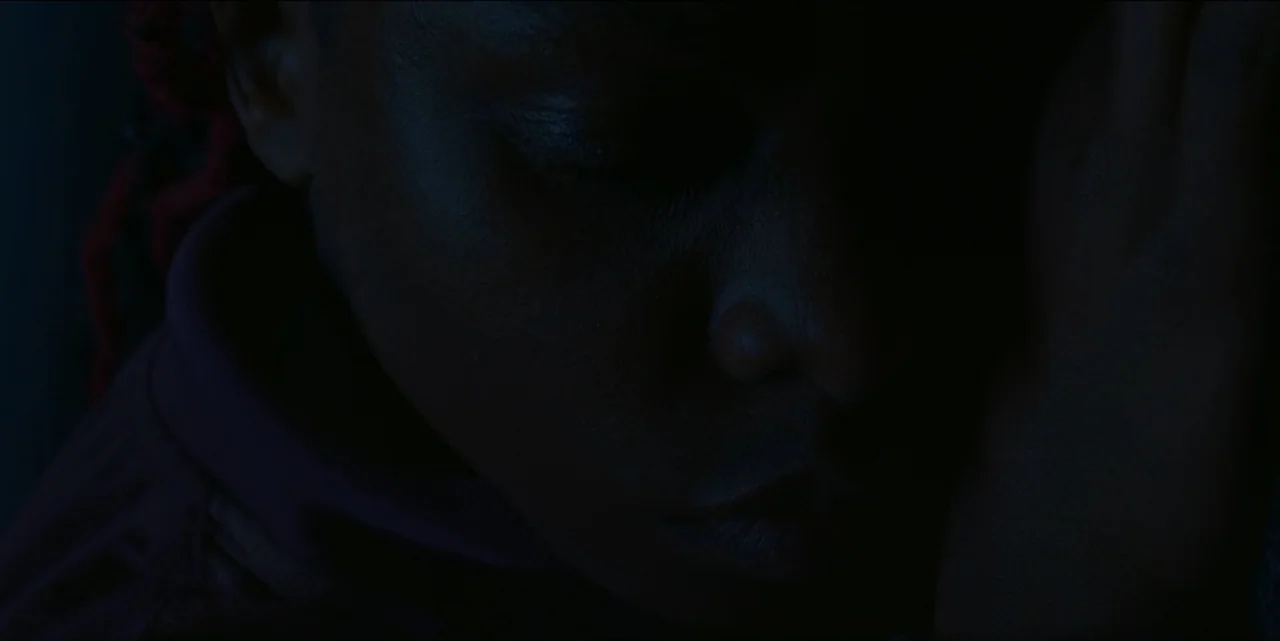 The Hunted (2024) movie still: closeup — A dark space focuses on the profile of a person resting their head. A person lies with their face turned…