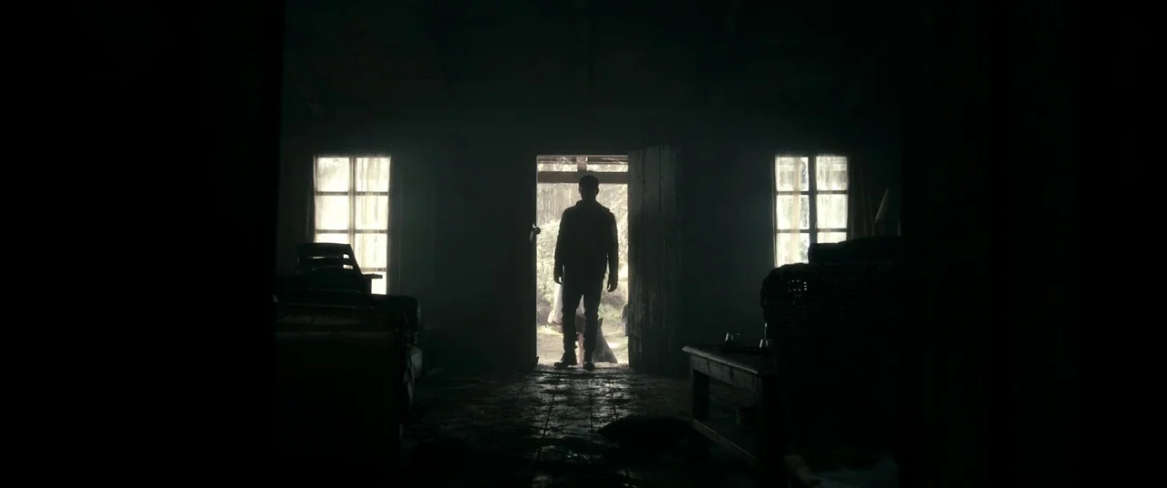 Evil Dead (2013) movie still: wide — A dark wooden room with two side windows and a central open door. A man stands in the doorway looking into the…