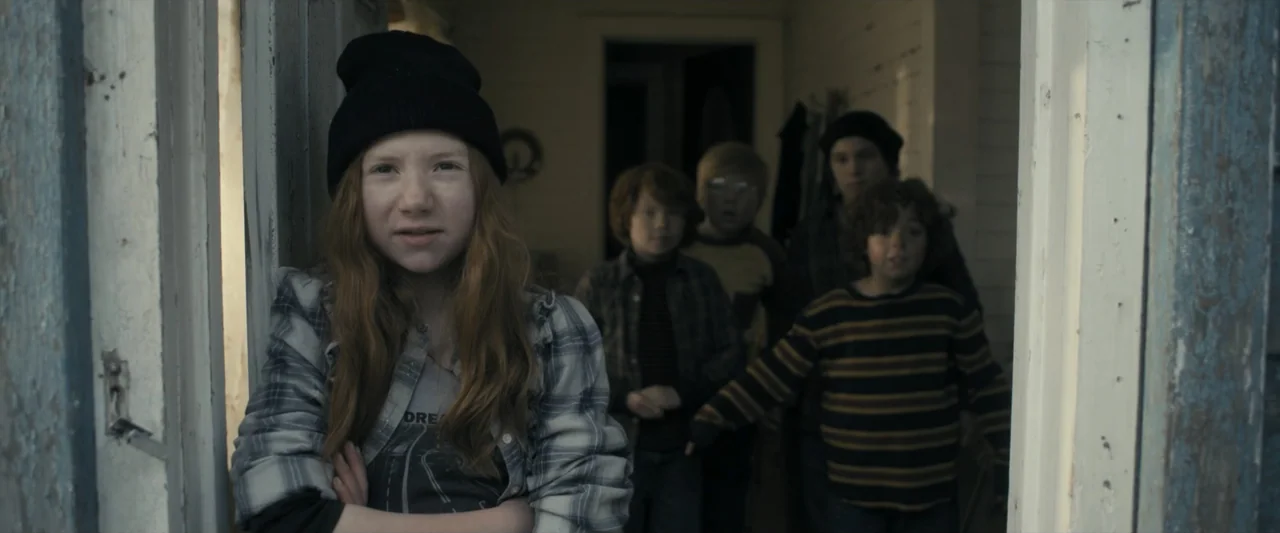 The Best Christmas Pageant Ever (2024) movie still: medium — A dimly lit interior hallway with white wooden panels and a visible doorway frame. A…