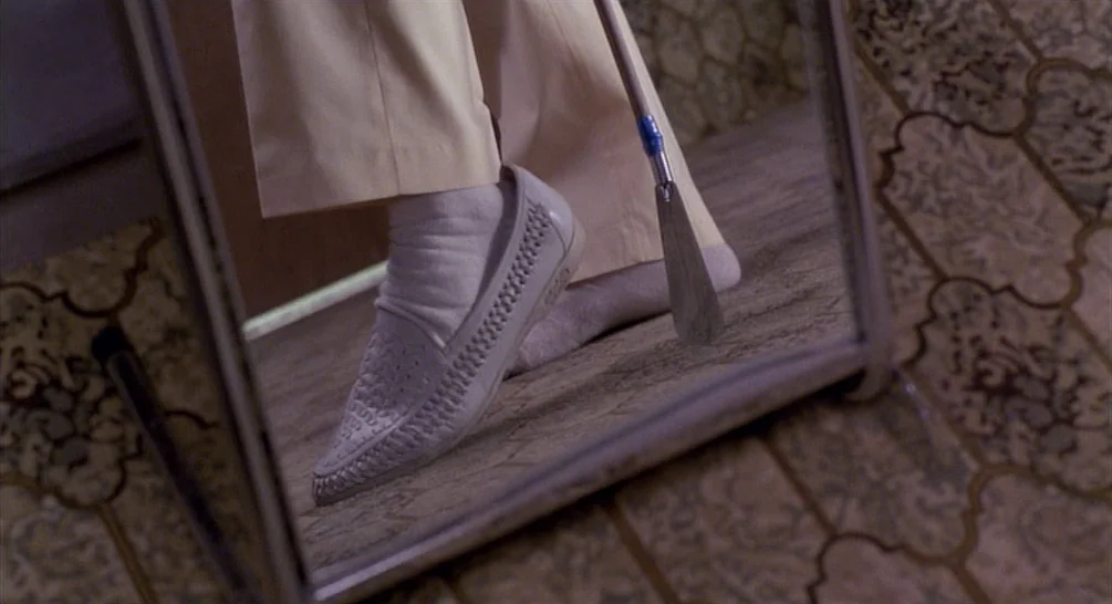 Raising Arizona (1987) movie still: closeup — A framed floor mirror reflects the lower body of an individual. The person wears cream-colored…