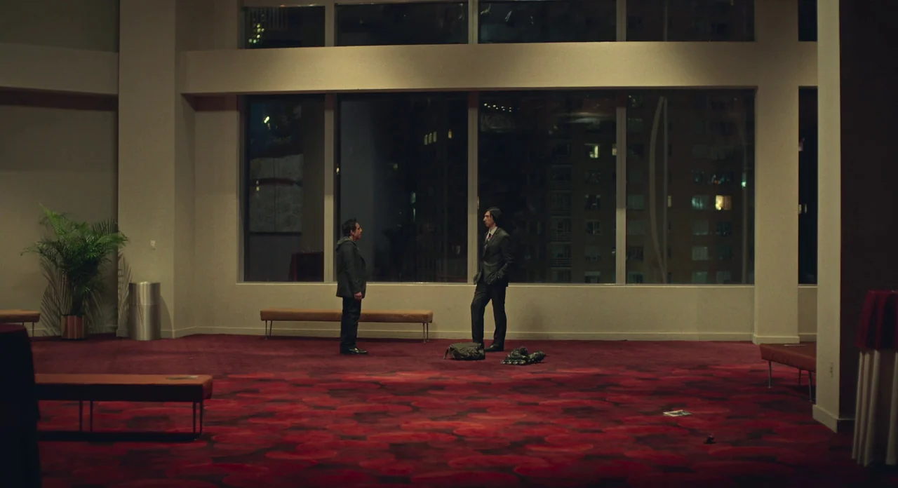 While We’re Young (2014) movie still: wide — An expansive, sparse lobby features a dark red patterned carpet and floor-to-ceiling windows. Two men…