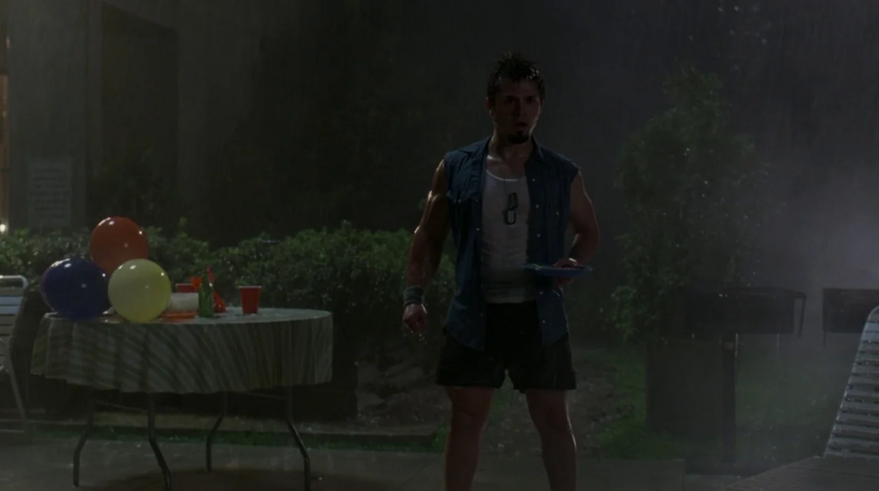 Lady in the Water (2006) movie still: fullbody — A rain-drenched patio at night features a table with party balloons and plastic cups. A young man…