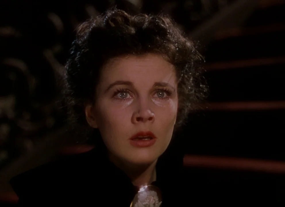 Gone with the Wind (1939) movie still: closeup — A dark staircase at night features a dark bannister and red-carpeted steps. A young woman with dark…