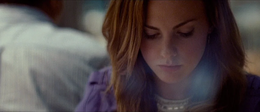 This Movie Is Broken (2010) movie still: closeup — A woman in a purple shirt sits at a table in a restaurant setting. She focuses her gaze downward…