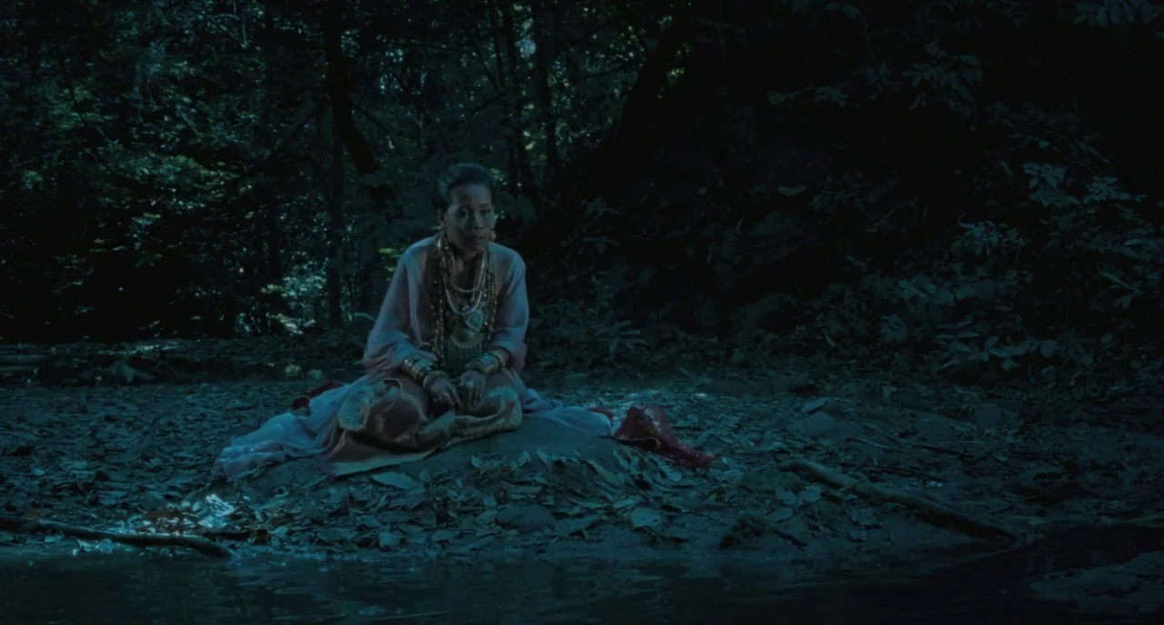 Uncle Boonme Who Can Recall His Past Lives (2010) movie still: medium — A woman sits on a dirt bank beside a dark, reflective stream at night.…