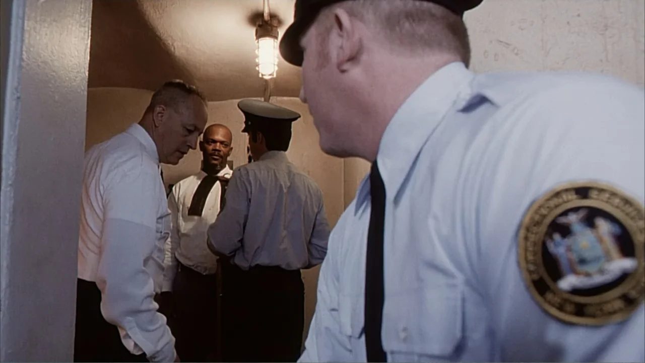 Against the Wall (1994) movie still: medium — A narrow institutional hallway has plain walls and an overhead fluorescent cage light. Three…