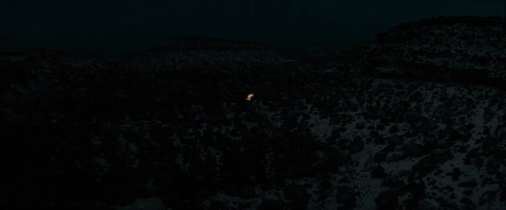 Let Me In (2010) movie still: establishing — A vast, dark, snow-covered landscape stretches under a moonless night sky. A tiny, isolated light…