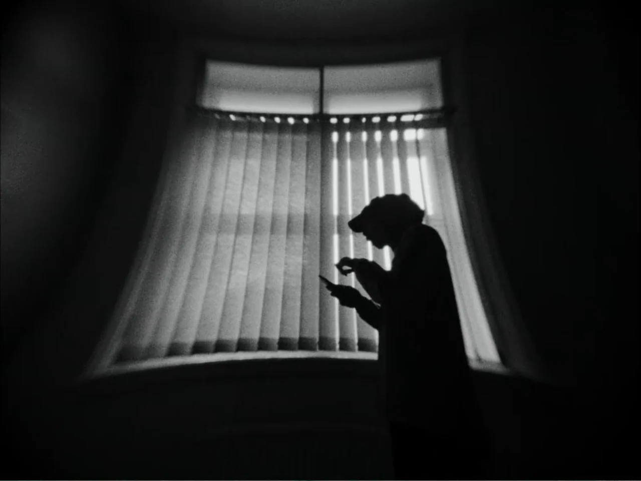As We Speak: Rap Music on Trial (2024) movie still: medium — A dark interior space features a large window with vertical blinds covering the glass.…