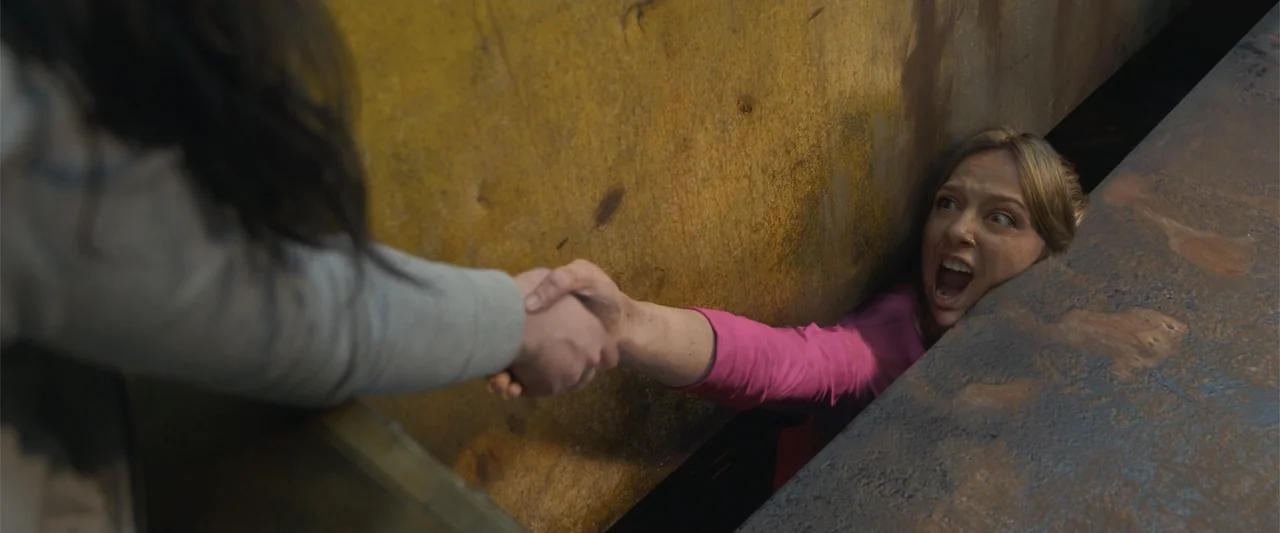 Final Destination Bloodlines (2025) movie still: medium — A woman is trapped in a narrow vertical space between two industrial rusted surfaces. She…